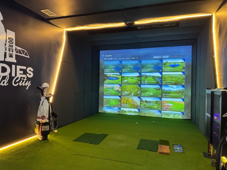 The same room finished as an RG simulator bay with turf, LED trim and the course menu on screen