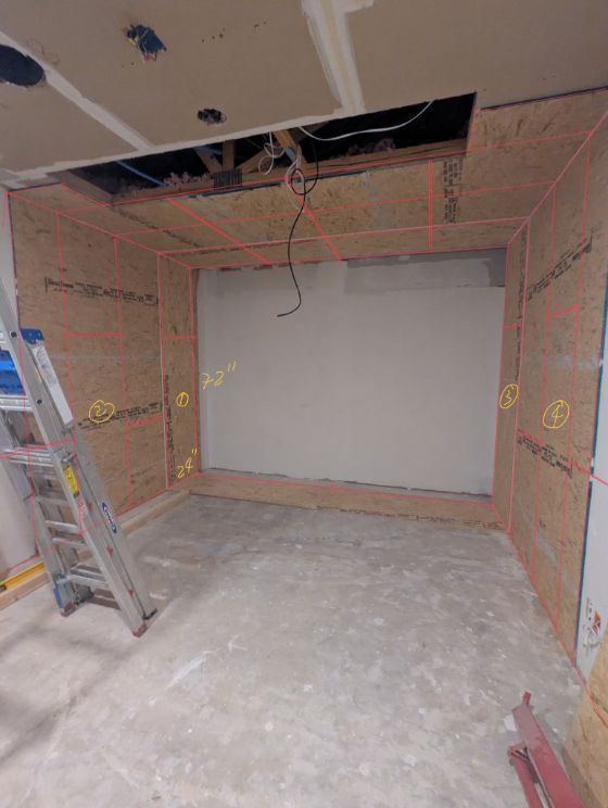 Framed room with bare plywood walls, an open ceiling and a ladder before the build