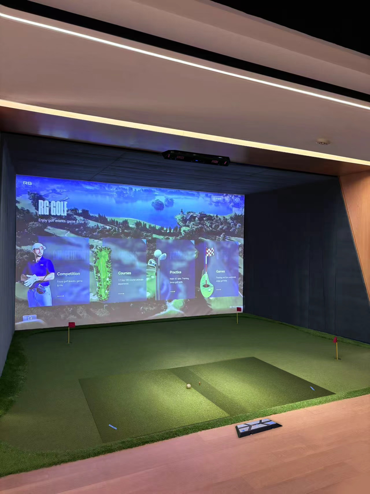 RG Golf Core Professional bay — projection screen running the English RG Golf software, ceiling triple-camera sensor, putting green and hitting mat